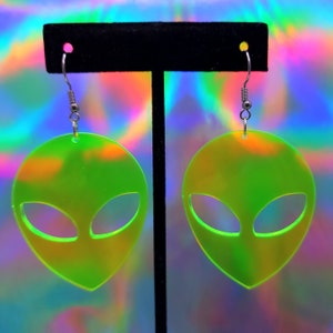 May include: A pair of green iridescent alien head-shaped earrings with silver hooks.