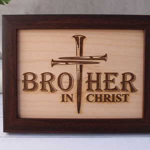 May include: A wooden sign with a brown frame, featuring a cross with nails and the text "BROTHER IN CHRIST".