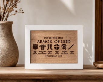 May include: A rectangular white frame containing a wooden plaque engraved with the text "PUT ON THE FULL ARMOR OF GOD" and "EPHESIANS 6:10". Below the text are six dark icons representing armor pieces labeled with their corresponding spiritual names.