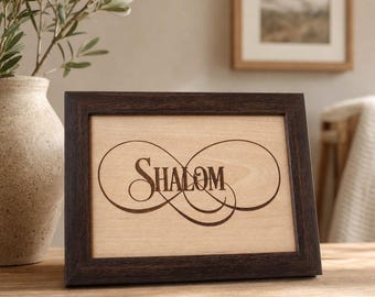 May include: A rectangular wooden frame with a dark brown finish containing a light-colored wooden insert. The insert features a laser-engraved infinity symbol design with the word SHALOM written in a decorative serif font across the center.
