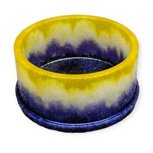 May include: A round resin container with a layered design. The top is bright yellow, fading to white, then deep blue. The container sits on a matching blue base. The interior is dark blue.