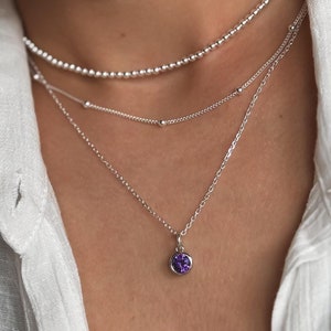 May include: A silver necklace with three chains and a small purple gemstone pendant.