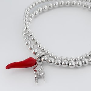 Può includere: Un braccialetto in argento con perline rotonde e un ciondolo a forma di peperoncino rosso. Il braccialetto è realizzato con perline piccole e rotonde ed è sovrapposto per un look elegante.