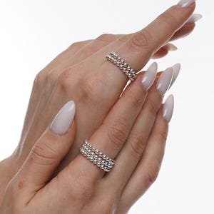 May include: A set of three silver beaded rings stacked on a finger. The rings are made of small, round beads that are evenly spaced.