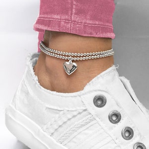 May include: Silver ankle bracelet with a heart charm. The bracelet is layered with two rows of small beads.