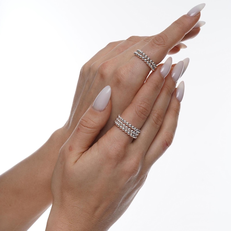 May include: A set of three silver beaded rings stacked on a finger. The rings are made of small, round beads that are evenly spaced.