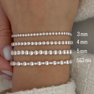 K&ouml;nnte beinhalten: Vier silberne Perlenarmb&auml;nder an einem Handgelenk. Die Armb&auml;nder bestehen aus unterschiedlich gro&szlig;en Perlen, wobei das obere Armband die kleinsten und das untere Armband die gr&ouml;&szlig;ten Perlen hat. Die Armb&auml;nder sind mit ihrer Perlengr&ouml;&szlig;e in Millimetern gekennzeichnet: 3 mm, 4 mm, 5 mm und 5 & 3 Mix.