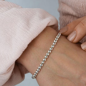 K&ouml;nnte beinhalten: Ein silbernes Armband mit einem schlichten Design. Das Armband besteht aus kleinen, runden Perlen, die auf einer d&uuml;nnen Kette aufgereiht sind.