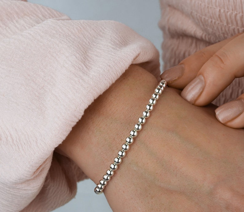 K&ouml;nnte beinhalten: Ein silbernes Armband mit einem schlichten Design. Das Armband besteht aus kleinen, runden Perlen, die auf einer d&uuml;nnen Kette aufgereiht sind.