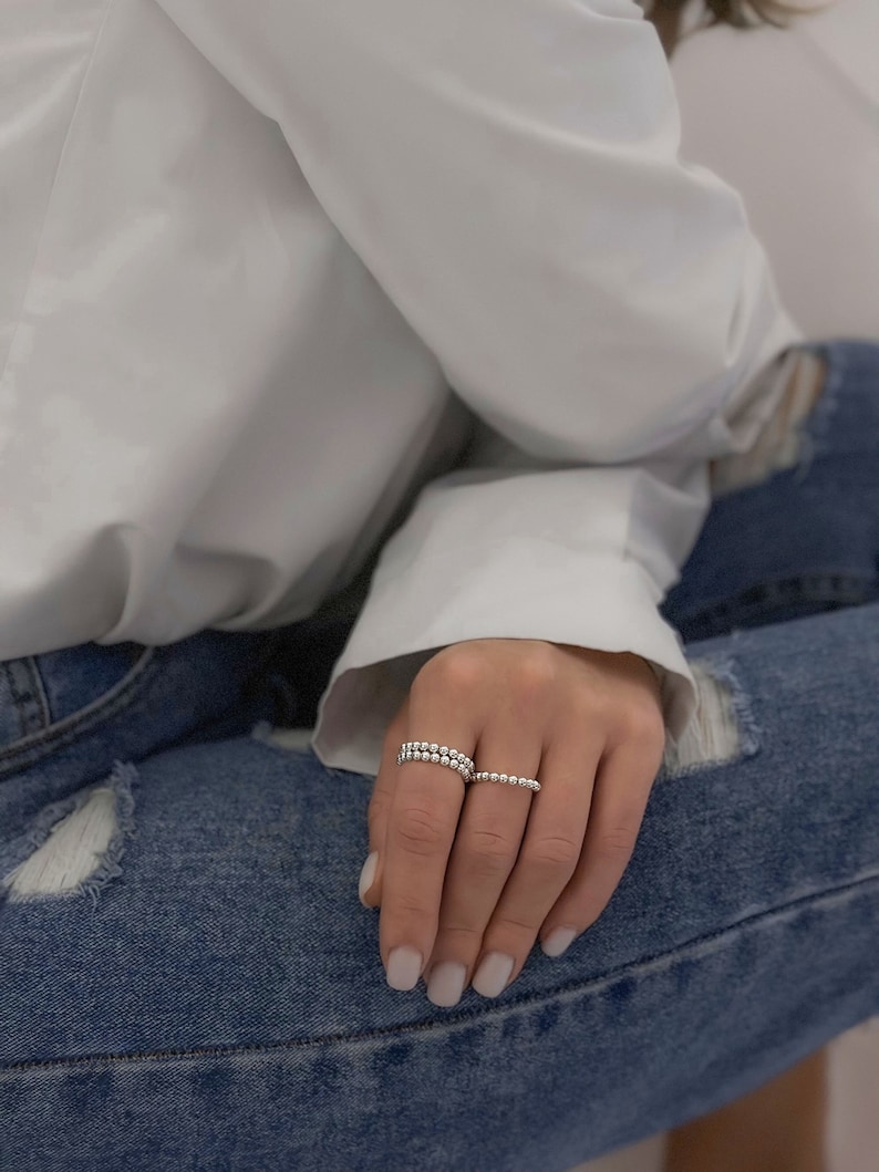 May include: Two silver beaded rings stacked on a finger. The rings are made of small, round beads.