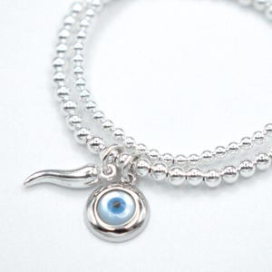 May include: A silver beaded bracelet with a charm featuring a blue evil eye and a silver horn.