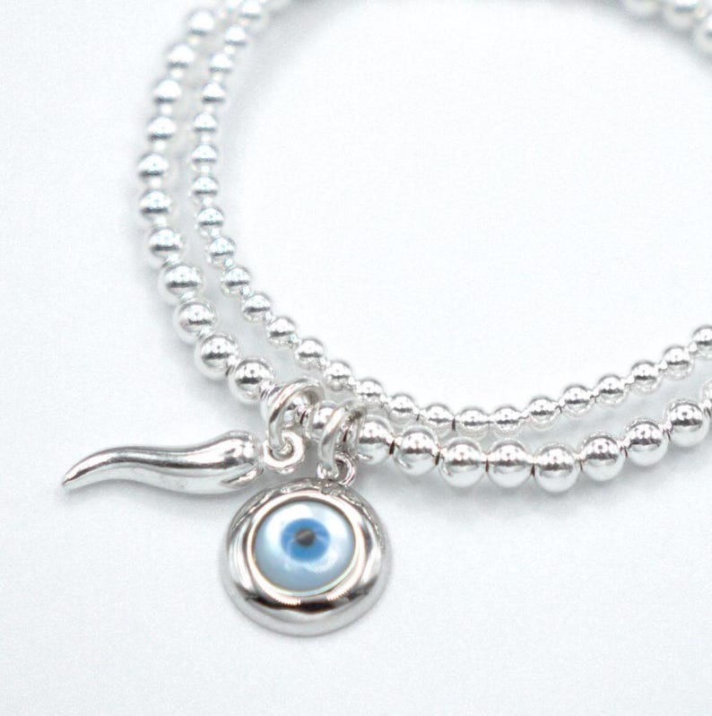 May include: A silver beaded bracelet with a charm featuring a blue evil eye and a silver horn.