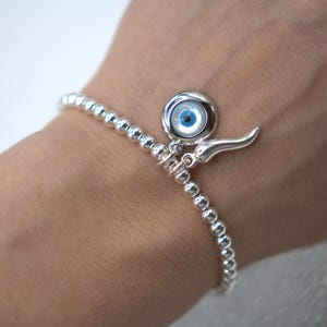 May include: A silver beaded bracelet with a charm featuring a blue evil eye and a silver horn pendant.