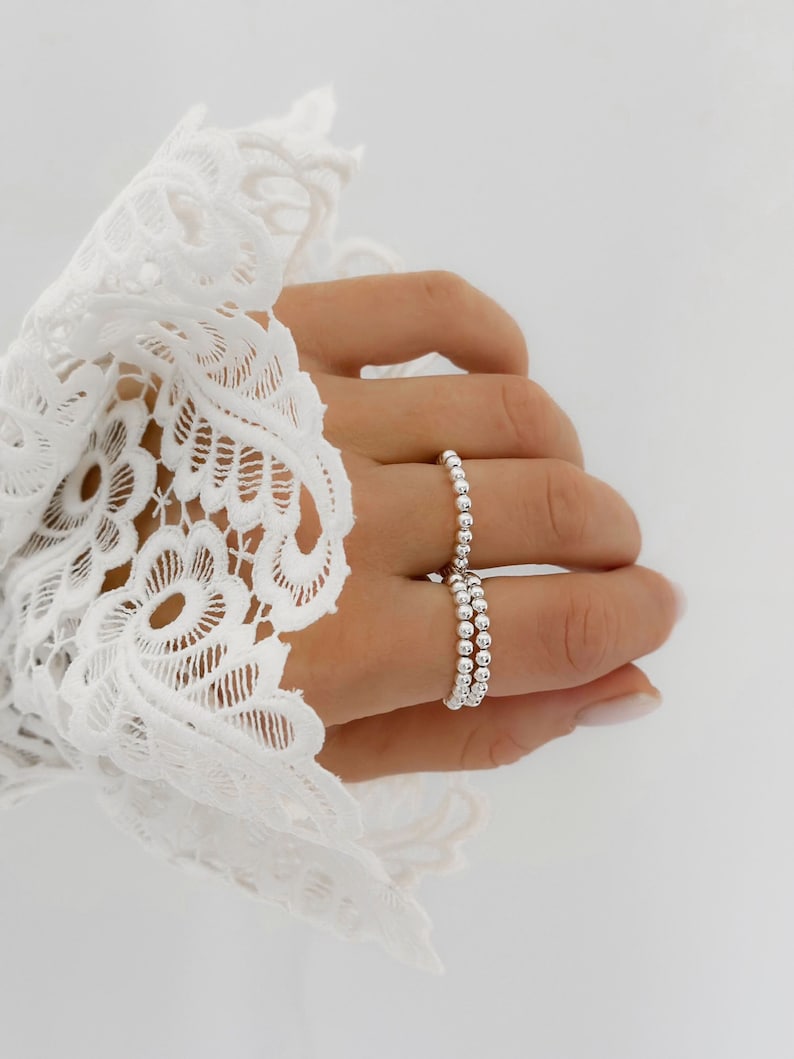 May include: A silver beaded ring with multiple bands stacked on a finger.