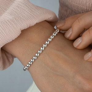 K&ouml;nnte beinhalten: Ein silbernes Armband mit einem schlichten Design. Das Armband besteht aus kleinen, runden Perlen, die gleichm&auml;&szlig;ig verteilt sind.