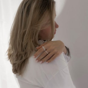May include: A woman wearing a white shirt with a silver ring on her finger. The ring is made of small, round beads.