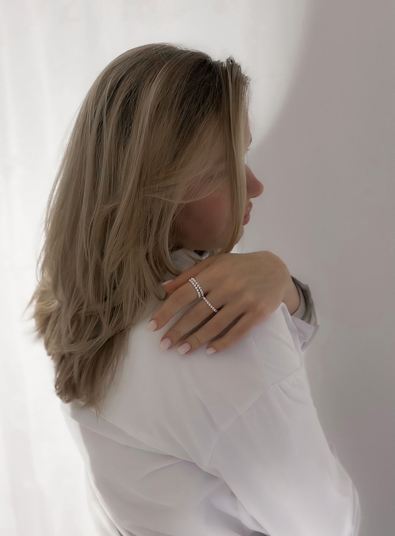 May include: A woman wearing a white shirt with a silver ring on her finger. The ring is made of small, round beads.