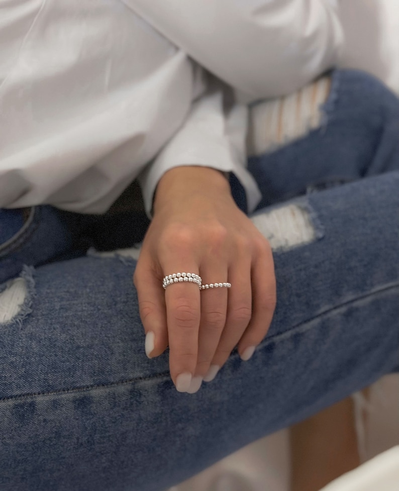 May include: Two silver beaded rings on a finger. The rings are stacked on top of each other.