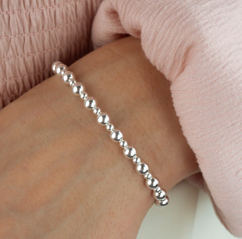 K&ouml;nnte beinhalten: Ein silbernes Armband mit einem schlichten Design. Das Armband besteht aus kleinen, runden Perlen, die auf einer d&uuml;nnen Kette aufgereiht sind.