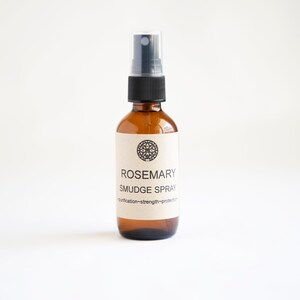 Pu&ograve; includere: Un flacone spray in vetro ambrato con erogatore in plastica nera ed etichetta beige. L'etichetta presenta un'icona geometrica circolare, il testo ROSEMARY SMUDGE SPRAY e le parole purification~strength~protection stampate in inchiostro nero.