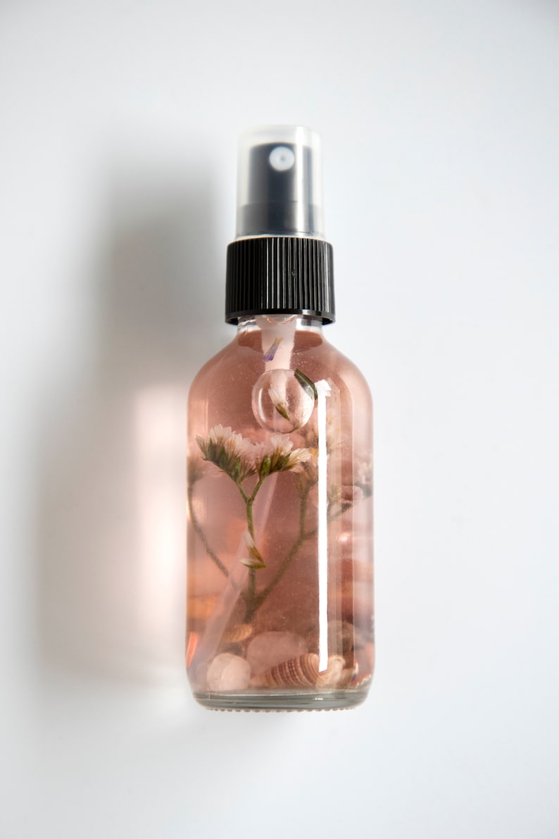 May include: A clear glass bottle with a black spray top filled with a pink liquid and dried flowers and seashells.
