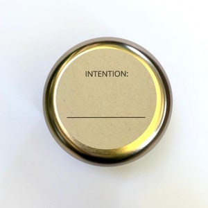 May include: A gold metal container with a round, cream-coloured label that says "INTENTION:" with a blank line underneath.
