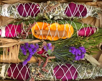 May include: A set of four smudge sticks in a cardboard box. The smudge sticks are wrapped in twine and decorated with dried flowers, orange slices, and cinnamon sticks.