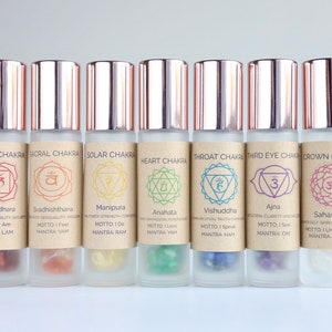 May include: Seven glass roller bottles with rose gold lids and labels. Each bottle is labeled with a different chakra name, symbol, and mantra. The chakras are Root, Sacral, Solar Plexus, Heart, Throat, Third Eye, and Crown.