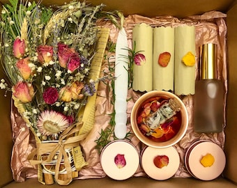 May include: A gift box filled with a variety of items, including a bouquet of dried flowers, a white candle, a small glass jar with dried herbs and petals, a bottle of clear liquid, and four small round containers with lids.