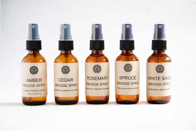 Pu&ograve; includere: Cinque flaconi spray in vetro ambrato con erogatori in plastica nera ed etichette beige. Le etichette presentano un'icona mandala circolare e il testo che identifica le fragranze come Amber, Cedar, Rosemary, Spruce e White Sage Smudge Spray.