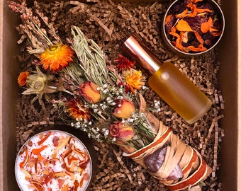 May include: A brown cardboard box with a dried flower bouquet, a small jar of dried flowers, a clear glass bottle with a copper top, and a small white candle with orange and yellow dried flowers inside.