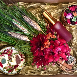Puede incluir: Una caja de regalo llena de un ramo de flores secas, una vela, una botella de líquido rojo y una pequeña lata de fruta y flores secas.