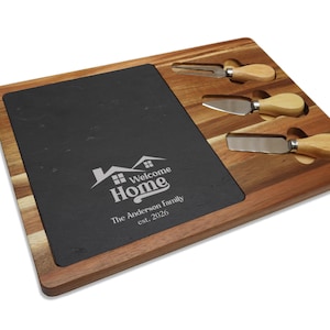 May include: A wooden cheese board with a black slate insert and three cheese knives. The board is engraved with "Welcome Home" and "The Anderson Family est. 2026". The board is made of acacia wood and is a perfect gift for housewarming.