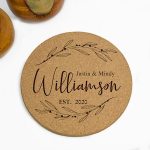 May include: A round cork coaster with a brown, engraved design of a leafy wreath with berries. The text "Justin & Mindy Williamson EST. 2020" is engraved in the center.