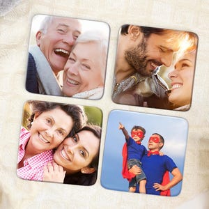 May include: Set of four square coasters, each featuring a different photograph. The images include a smiling older couple, a couple gazing at each other, two smiling women, and a father and son dressed as superheroes.