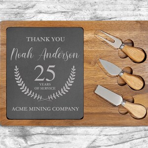May include: A wooden cheese board with a slate insert. The slate is engraved with "Thank You Noah Anderson 25 Years of Service" and "Acme Mining Company." Three cheese knives with wooden handles are included.