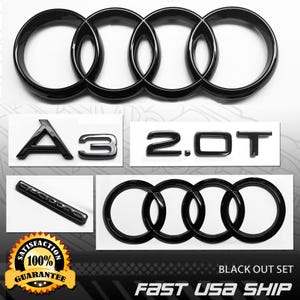 May include: A set of glossy black automotive emblems including two four-ring logos, an A3 badge, a 2.0T badge, and a quattro badge. The items are presented on a white background with a yellow and black satisfaction guarantee seal in the corner.