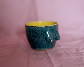 Ceramic stoneware small coffee or tea cup in body form shape. Boob/breast/tit ceramic glazed with glossy dark green-blue and yellow