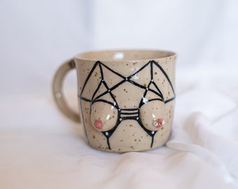 Stoneware ceramic boob mug with strappy harness lingerie in black on spotted clay with handle. Body tit/breast coffee/tea cup