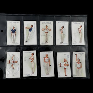 May include: A collection of vintage cigarette cards featuring illustrations of men performing various exercises. The cards are displayed in a clear plastic holder. Each card has the text "WILLEY'S CIGARETTES" printed on it.