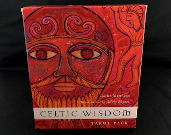 May include: A red tarot card box with a Celtic theme. The box features a stylized illustration of a face with a large mustache and beard. The text "Celtic Wisdom Tarot Pack" is displayed on the front.