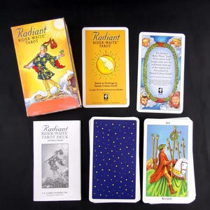 May include: A Radiant Rider-Waite tarot deck set including a box with a figure illustration, an instruction booklet, and several cards. The cards feature a yellow sun design, a blue back with yellow stars, and a Six of Wands card illustration.