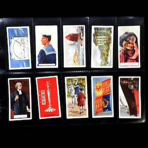 May include: A collection of vintage trading cards in a black album. The cards feature various images, including a sailor, a building, a flag, and a ship. The cards are in good condition and would be a great addition to any collection.