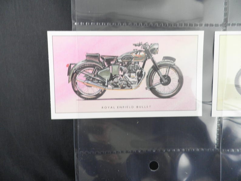 Puede incluir: Ilustraci&oacute;n de una motocicleta Royal Enfield Bullet en una tarjeta. La moto est&aacute; representada en tonos grises y verdes, sobre un fondo rosa. El texto "ROYAL ENFIELD BULLET" est&aacute; impreso debajo de la imagen.