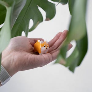 May include: A small ceramic figurine of a Shiba Inu dog. The figurine is orange and white and has a cute expression.