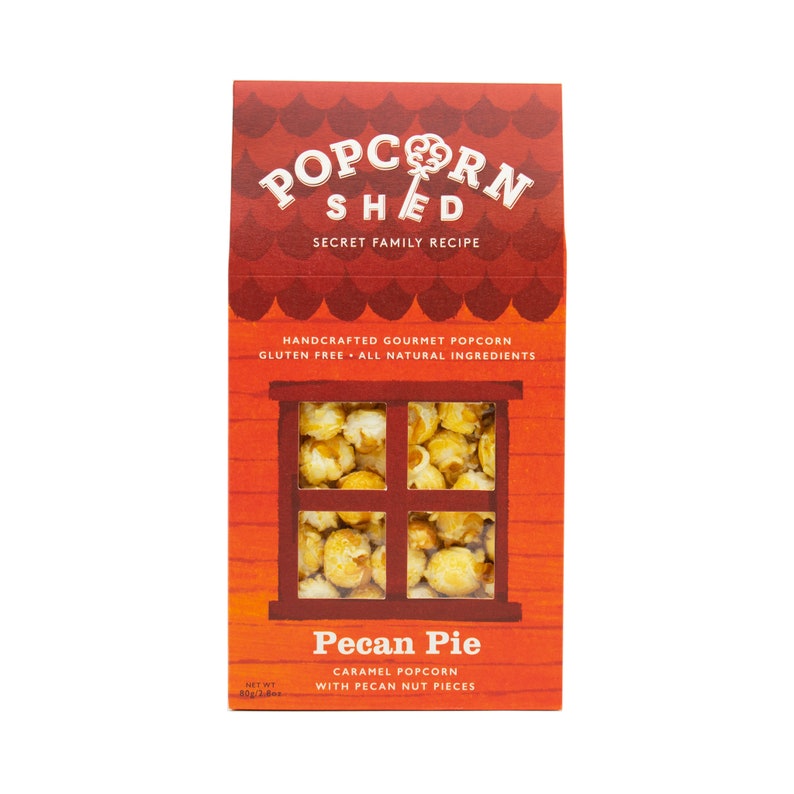 May include: A red and orange box with a window showing caramel popcorn with pecan pieces. The box says "Popcorn Shed" and "Pecan Pie Caramel Popcorn with Pecan Nut Pieces".