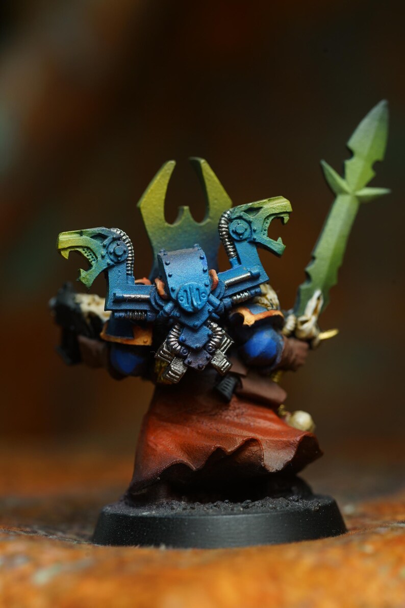 Op de afbeelding: Miniatuurfiguur van een krijger in blauw pantser met groene accenten, met een groen zwaard. De figuur heeft een rode mantel en een geel en groene hoofdtooi. De basis is zwart.