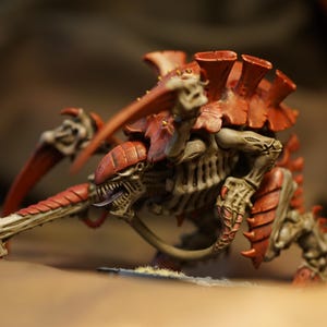 Puede incluir: Figura en miniatura detallada de una criatura Tiránida, con armadura roja y color hueso. El modelo tiene garras afiladas, una cabeza larga y una boca amenazante abierta, mostrando detalles intrincados.