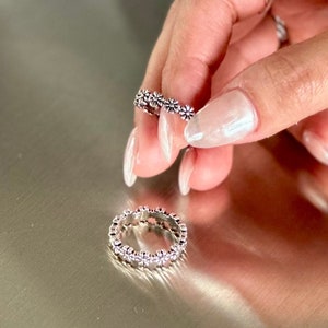 Puede incluir: Dos anillos de plata con un diseño de margarita. Los anillos están sobre una superficie plateada.