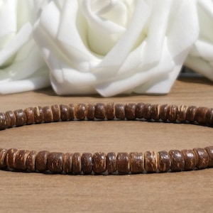 May include: A brown coconut shell bead necklace. The necklace is made of small, round beads that are strung together on a thin cord. The beads are a natural brown colour and have a slightly rough texture.